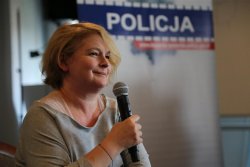 Dominika Ostałowska z mikrofonem, na tle baneru z napisem &quot;Policja&quot;