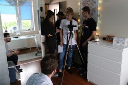 Grupa młodzieży w prywatnym mieszkaniu w trakcie realizowania zdjęć przy pomocy aparatu fotograficznego na statywie.