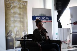 Magdalena Boczarska w fotelu w trakcie spotkania z młodzieżą, w tle banery Policja oraz Camerimage.