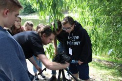 Młodzież z wykładowcą (Jan Holoubek) realizuje zdjęcia w parku, w tle zbiornik wodny i drzewa.